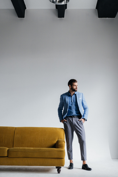 stylish man in blue suit posing at yellow couch - Foto, Bild