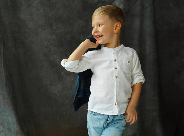 Portret van smiley mooie jongetje in spijkerbroek over grijs textiel  - Foto, afbeelding