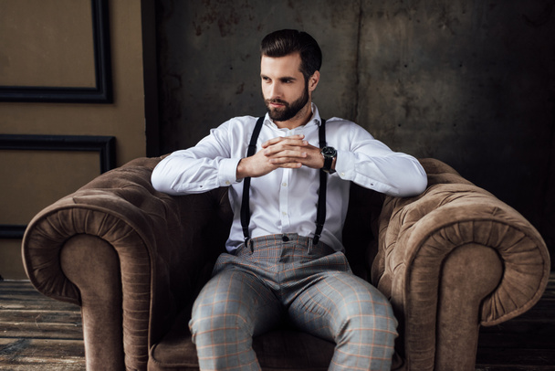 pohledný muž módní myšlení a sedí v křesle  - Fotografie, Obrázek