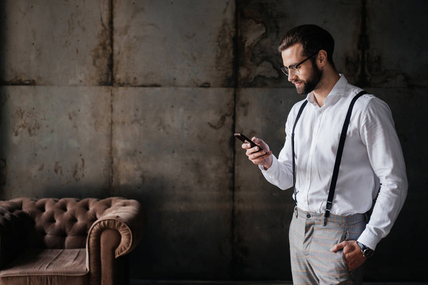 fashionable bearded man in suspenders using smartphone - Photo, Image