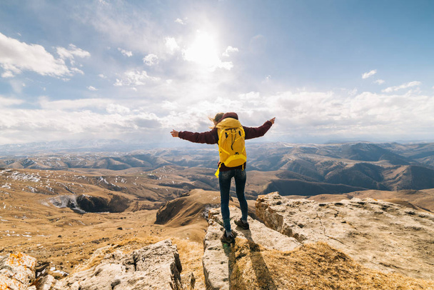 active young girl with a yellow backpack travels through the Caucasus mountains, enjoys nature, raised her hands upwards - Φωτογραφία, εικόνα