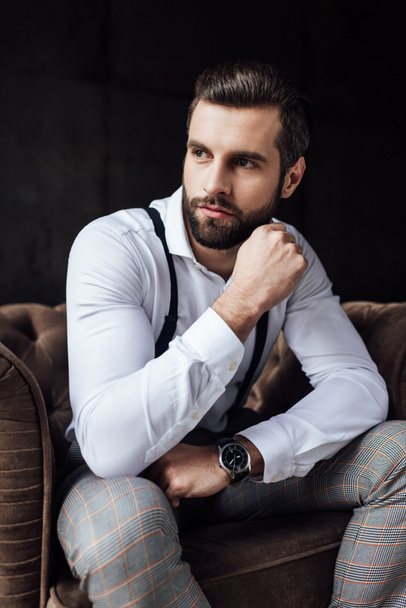 stylish man in suspenders thinking and sitting in armchair  - Photo, Image