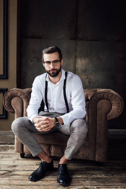 fashionable man in glasses and suspenders sitting in armchair  - Φωτογραφία, εικόνα