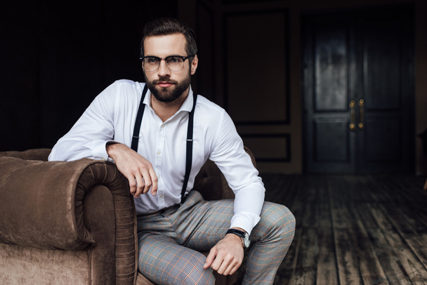 moda sakallı adam gözlük ve koltukta oturan jartiyer  - Fotoğraf, Görsel