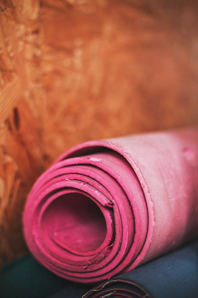 Old used bright pink gym mat rolled on a blurred wooden panel wall background. - Photo, image