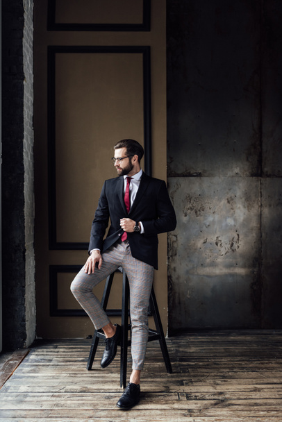 handsome fashionable businessman in suit posing on stool in loft interior  - Foto, Imagem