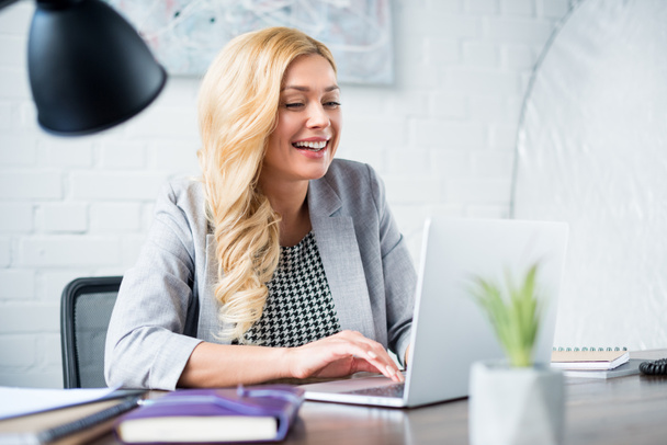 smiling businesswoman using laptop at work - Fotó, kép