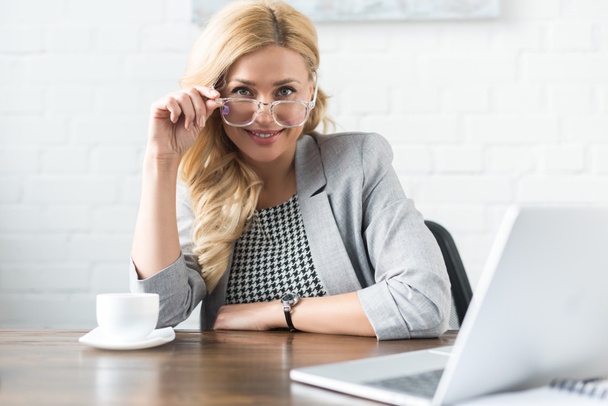 smiling businesswoman looking at camera above glasses - Foto, Imagem