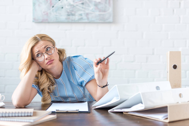 tired businesswoman holding pen and sitting at table with documents - Foto, Imagem