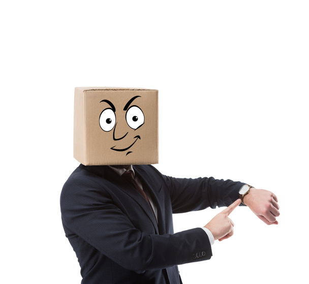 zakenman met kartonnen doos op hoofd wijzend op polshorloge geïsoleerd op wit  - Foto, afbeelding