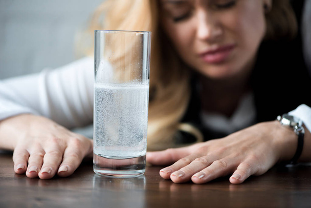 businesswoman with headache sitting near glass of water with medicines - Foto, afbeelding