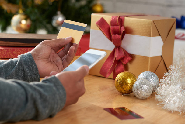 Kädet mies käyttää älypuhelinta ja luottokorttia ostaa joululahjoja
 - Valokuva, kuva