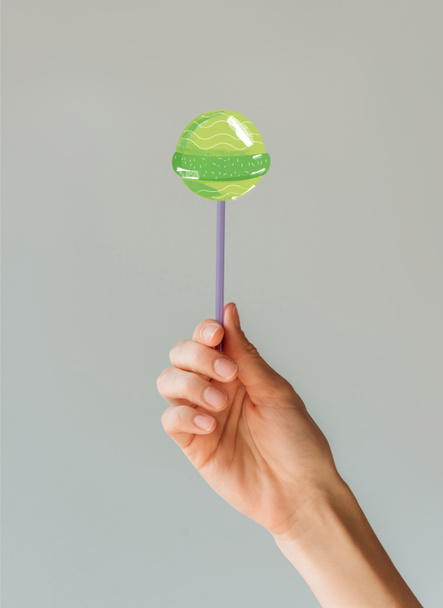 Cropped image of woman holding green lollipop in her hand isolated on gray  - Fotó, kép