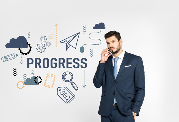 stylish young businessman standing with hand in pocket and talking on smartphone while looking away isolated on grey, progress icons - Foto, Imagen