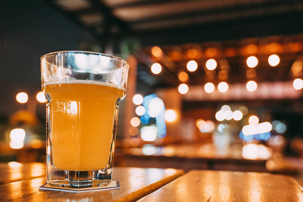 One pint of beer on restaurant table with copy space on blur bokeh background. Happy event celebrations, nightlife at pub, dinner party, or alcoholic drinks advertisement concept - Photo, Image