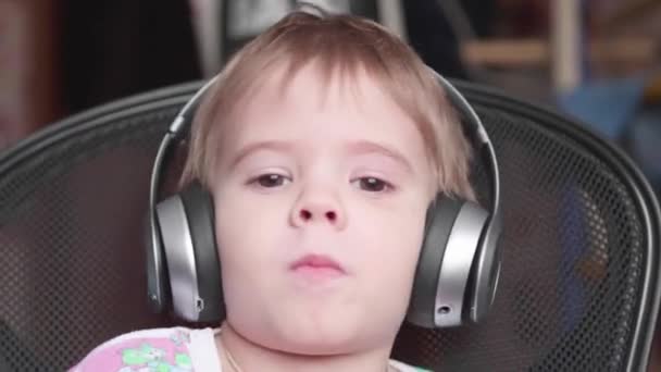 A little funny boy sits in a chair and listens to music through headphones. Face close up - Footage, Video