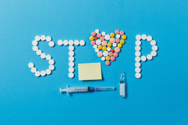 İlaç beyaz, renkli yuvarlak tabletler üzerinde Stop izole Word'de arka plan mavi. Hapları ampul şırınga iğne, boş kağıt etiket sayfası kalp. Sağlık tedavi seçimi, sağlıklı yaşam kavramı. - Fotoğraf, Görsel