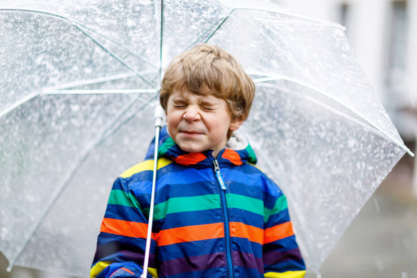 Niño rubio camino a la escuela caminando durante el aguanieve, la lluvia y la nieve con un paraguas en el día frío
 - Foto, Imagen