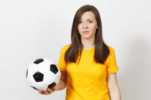 Красивая европейская грустная молодая расстроенная женщина, футбольный фанат или игрок в желтой форме держит футбольный мяч, беспокоясь о потере команды изолированы на белом фоне. Спорт, футбол, концепция образа жизни
. - Фото, изображение