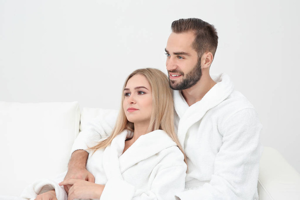 Jovem casal em roupões de banho relaxante no sofá
 - Foto, Imagem