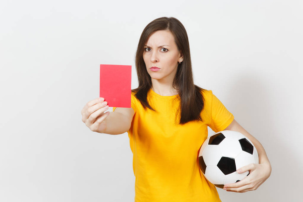 europäische ernste junge Frau, Fußballschiedsrichterin oder Spielerin in gelber Uniform, die die rote Karte zeigt und den Ball isoliert auf weißem Hintergrund hält. Sport, Fußball spielen, gesunder Lebensstil. - Foto, Bild