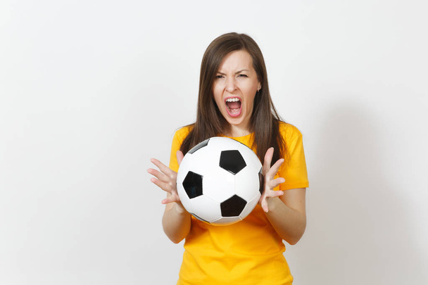 Красивая европейская молодая сердитая кричащая женщина, футбольный фанат или игрок в желтой форме, держащий футбольный мяч изолирован на белом фоне. Спорт, футбол, здоровье, концепция здорового образа жизни
. - Фото, изображение