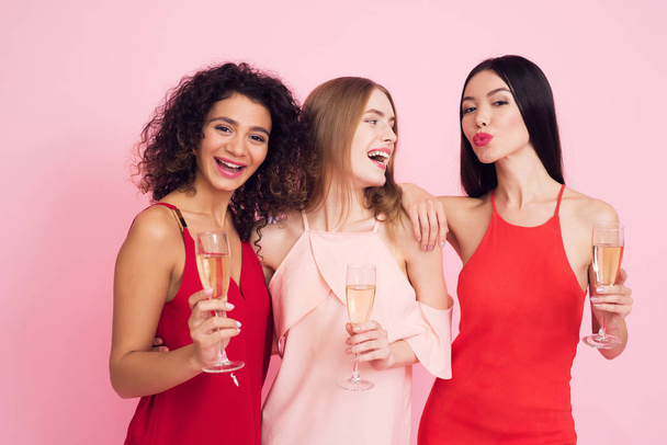 Three girls in white and red dresses with champagne on pink background celebrating women's day March 8. - Fotoğraf, Görsel