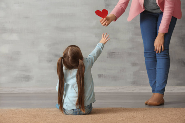 Woman giving heart to sad little girl indoors. Psychological support - Фото, зображення