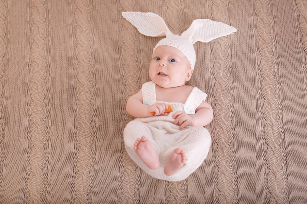 Cute little baby in bunny costume with carrot lying on plaid, top view - Zdjęcie, obraz