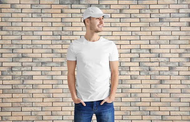 Young man in stylish t-shirt against brick wall. Mockup for design - Foto, Bild