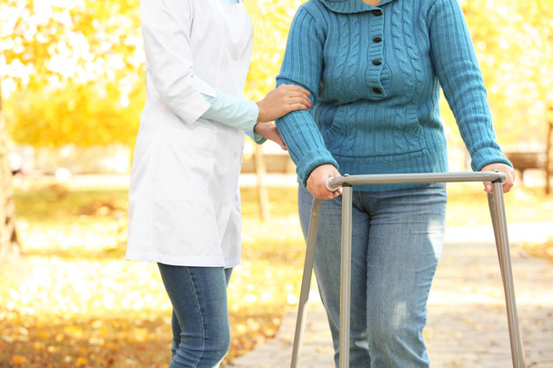 Senior woman with walking frame and young caregiver in park - Foto, afbeelding