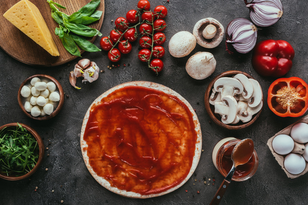 top view of uncooked pizza dough with sauce and vegetables on concrete table - Foto, imagen