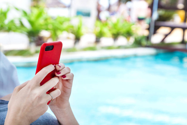Dziewczyna na leżaku w pobliżu basenu z nowoczesnym telefonie komórkowym (smartfonie) w jej ręce (z miejsca kopii)  - Zdjęcie, obraz