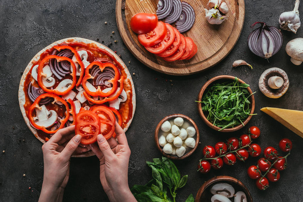 Plan recadré d'une femme étalant des tranches de poivron sur une pizza sur une table en béton - Photo, image