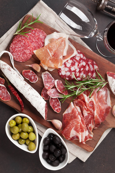 Salami, jambon tranché, saucisse, prosciutto, bacon, olives, pain et verre de vin rouge. Assiette antipasto viande sur table en pierre. Vue du dessus
 - Photo, image