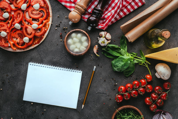 vista superior de la pizza sin cocer con cuaderno en blanco para la receta en la mesa de hormigón
 - Foto, imagen