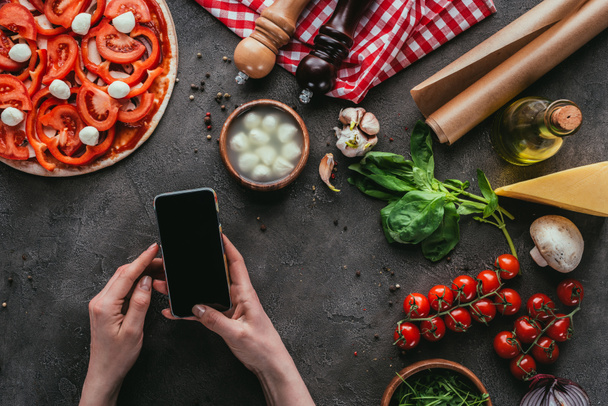 plan recadré de femme en utilisant un smartphone tout en préparant une pizza sur une table en béton
 - Photo, image