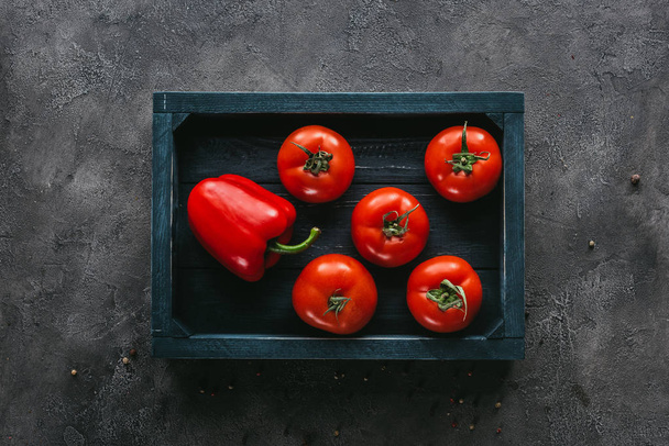 top view of tomatoes and bell pepper in box on concrete surface - Foto, Bild