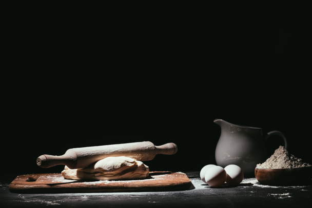 dough with ingredients and rolling pin on black - Фото, изображение
