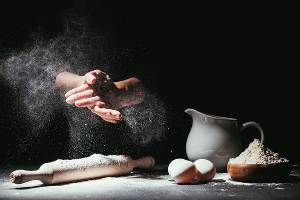 cropped shot of chef clapping ahnds with flour before making dough on black - Photo, Image