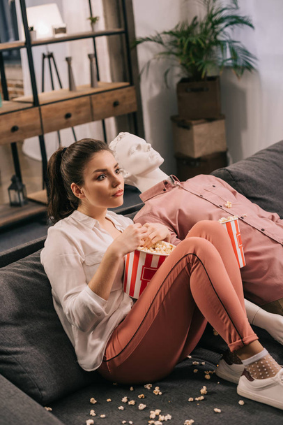 woman eating popcorn while watching film together with manikin at home, perfect relationship dream concept - Photo, Image
