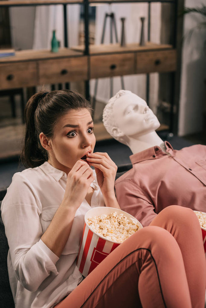 scared woman eating popcorn while watching film together with manikin at home, perfect relationship dream concept - Photo, Image