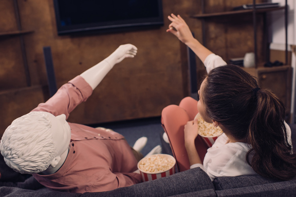 Achteraanzicht van vrouw popcorn eten tijdens het kijken naar de film samen met de proefpop thuis, perfecte relatie droom concept - Foto, afbeelding