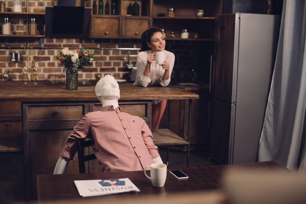 enfoque selectivo de la mujer joven con taza de café y maniquí en la mesa en la cocina, concepto de sueño relación perfecta
 - Foto, Imagen