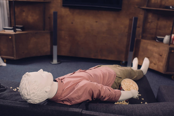 εκλαϊκευμένη κούκλα σε casual ρούχα ξαπλωμένη στον καναπέ με ποπ-κορν - Φωτογραφία, εικόνα