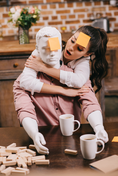 Portret van een vrouw met sticky note op voorhoofd knuffelen leek pop thuis, perfecte relatie droom concept - Foto, afbeelding