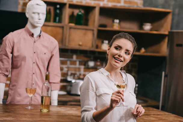 selective focus of woman with glass of wine and manikin in casual clothing in kitchen at home, unrequited love concept - Photo, Image