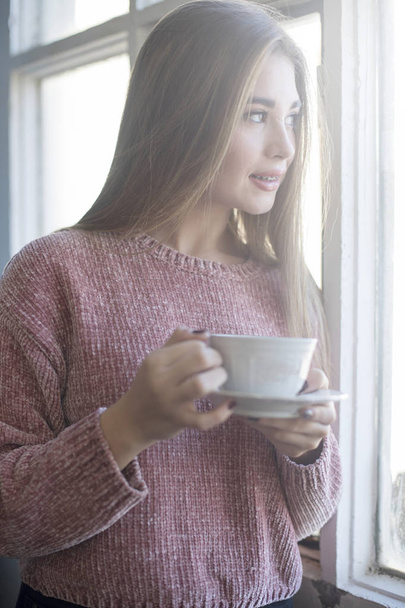 Красивая женщина смотрит в окно, держа чашку чая
 - Фото, изображение