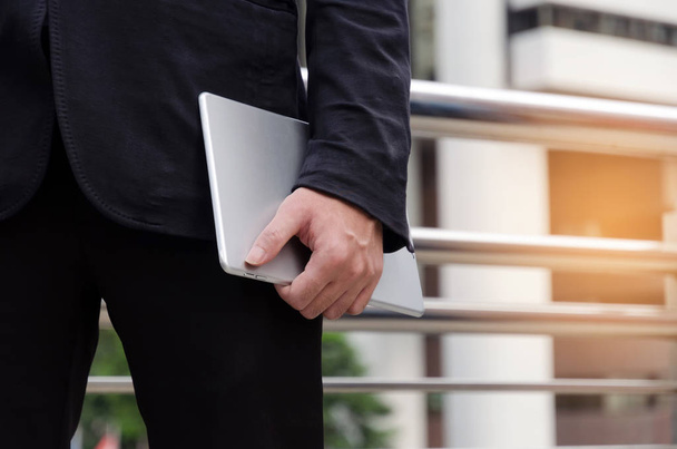 Dłoń biznes przystojny mężczyzna w czarnym garniturze, trzymając telefon tablet komputer stojący w tle nowoczesne miasto, połączenie sieci z Internetem, Technologia komunikacji i finansowych koncepcja z bliska - Zdjęcie, obraz