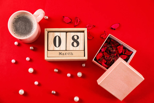 Wooden block calendar, flower petals and cup of coffee on color background. International Women's Day celebration - 写真・画像